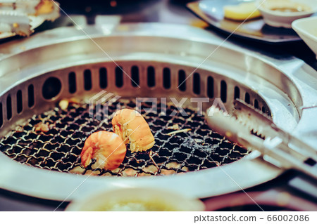 People grilling meat on a smokeless barbecue grill in a restaurant. Selective focus on shrimps. 66002086