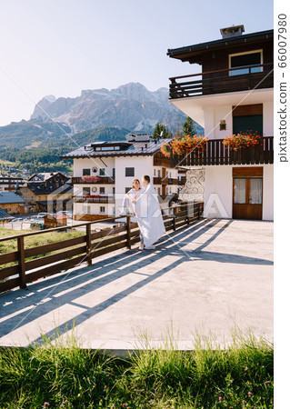 A guy and a girl cuddle with a blanket outside a hotel in the mountains. Cortina Ampezzo is an Italian city in province of Belluno in Veneto region, a winter resort in Dolomites A guy and a girl cuddle with a blanket outside a hotel in the mountains. Cortina Ampezzo is an Italian city in province of Belluno in Veneto region, a winter resort in Dolomites 66007980