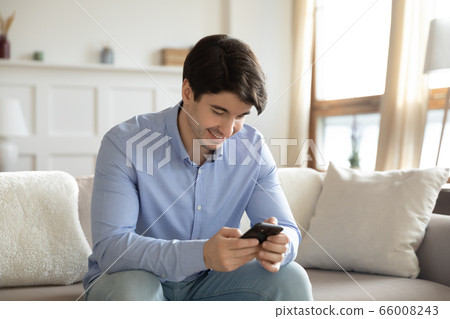 Smiling young man using modern smartphone at home Smiling young man using modern smartphone at home 66008243