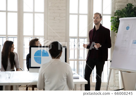 Male speaker presenting marketing strategy on flipchart to concentrated colleagues. Male speaker presenting marketing strategy on flipchart to concentrated colleagues. 66008245