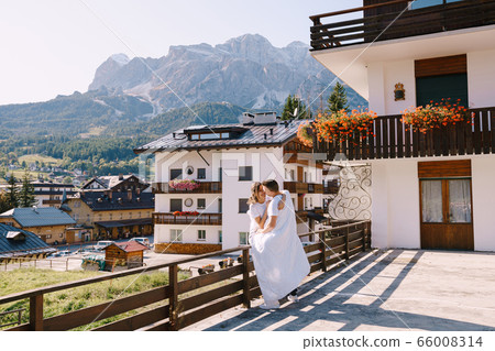 A guy and a girl cuddle with a blanket outside a hotel in the mountains. Cortina Ampezzo is an Italian city in province of Belluno in Veneto region, a winter resort in Dolomites A guy and a girl cuddle with a blanket outside a hotel in the mountains. Cortina Ampezzo is an Italian city in province of Belluno in Veneto region, a winter resort in Dolomites 66008314