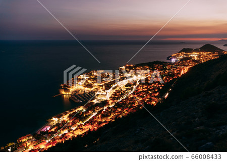 Aerial top night view on the old city of Dubrovnik, from the observation deck on the mountain above the city. Film location. The view of the city is based on the Royal Harbor. Aerial top night view on the old city of Dubrovnik, from the observation deck on the mountain above the city. Film location. The view of the city is based on the Royal Harbor. 66008433