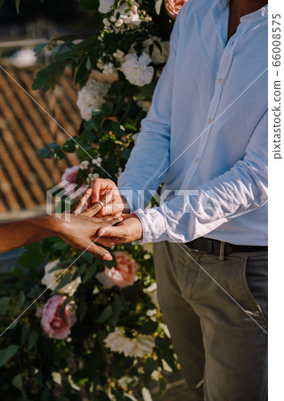 Interracial wedding couple - African-American bride and Caucasian groom. Groom puts a ring on brides finger. Destination fine-art wedding in Florence, Italy. Wedding ceremony on the roof Interracial wedding couple - African-American bride and Caucasian groom. Groom puts a ring on brides finger. Destination fine-art wedding in Florence, Italy. Wedding ceremony on the roof 66008575