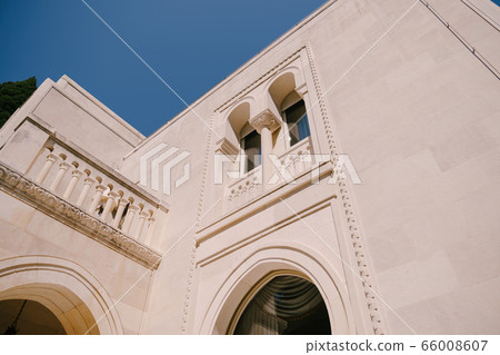 The white facade of the building with arched windows and columns on the balconies, against the blue sky. The white facade of the building with arched windows and columns on the balconies, against the blue sky. 66008607