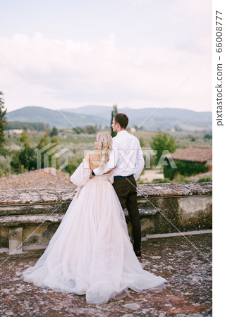 Wedding at an old winery villa in Tuscany, Italy. A wedding couple stands on the roof of an old winery, cuddles, stands with his back to the frame. Wedding at an old winery villa in Tuscany, Italy. A wedding couple stands on the roof of an old winery, cuddles, stands with his back to the frame. 66008777