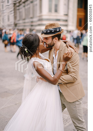 Multiracial wedding couple. African-American bride and Caucasian groom kissing among the crowd in Piazza del Duomo. Wedding in Florence, Italy 66008845
