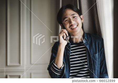Asian male entrepreneur standing inside window and talking mobile phone 66012899