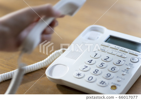 一隻女人的手拿起座機電話的聽筒 66017077
