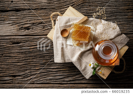 Honey bee in jar and honeycomb with honey dipper and flower on wooden table, bee products by organic natural ingredients concept, copy space for your text Honey bee in jar and honeycomb with honey dipper and flower on wooden table, bee products by organic natural ingredients concept, copy space for your text 66019235