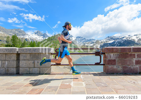 Mountain runner passes over an alpine dam 66019283