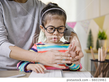 Mom teaching her daughter to writing in the book on the table, Educational concept for school Mom teaching her daughter to writing in the book on the table, Educational concept for school 66019461