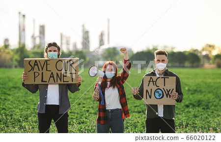 Group of young activists with placards standing outdoors by oil refinery, protesting. Group of young activists with placards standing outdoors by oil refinery, protesting. 66020122