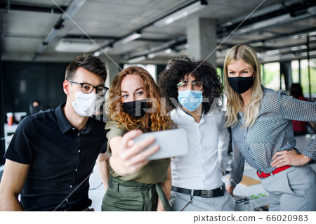 Young people with face masks back at work in office after lockdown, taking selfie. 66020983