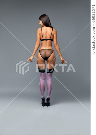The body of a young and beautiful woman in female underwear showing lingerie to the camera, isolated on a gray background. Fashion concept, copy space. 66021571