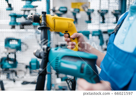 Worker holds two electric drills in tool store 66021597