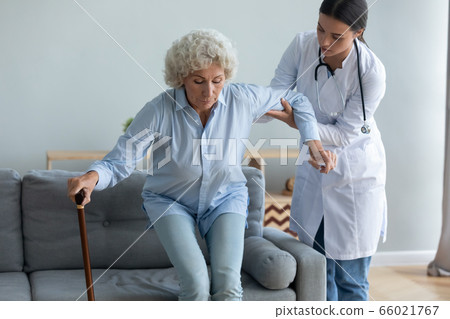Caring nurse helping to elderly woman get off the couch 66021767