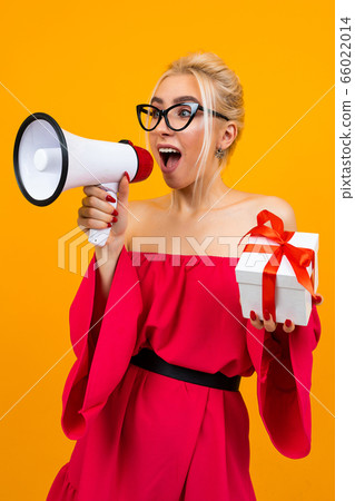 blond girl in a red dress talks about a draw with a megaphone and a gift box in hands on a yellow background 66022014