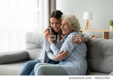 Elderly grandmother snuggle to grownup granddaughter seated on couch Elderly grandmother snuggle to grownup granddaughter seated on couch 66022065