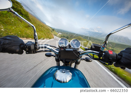 Motorcycle driver riding in Alpine highway, 66022350