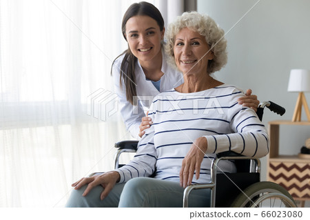 Caring nurse hug elderly disabled woman in wheelchair posing indoors 66023080