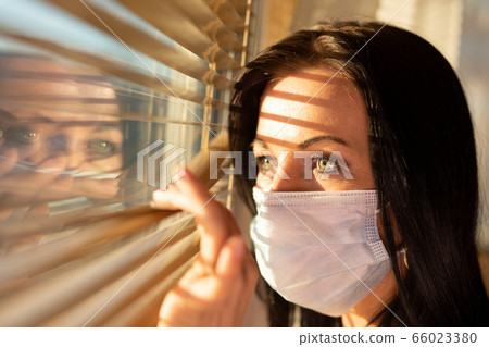 Woman with veil looking out of home window, 66023380