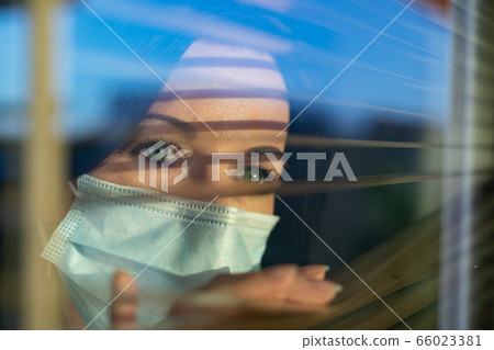 Woman with veil looking out of home window, 66023381