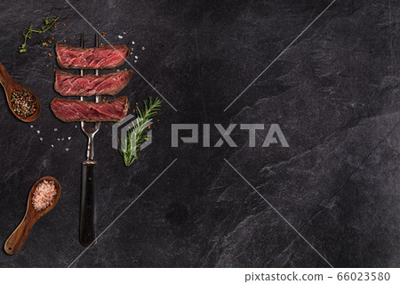 Grilled beef steak on black stone table. Top view. 66023580