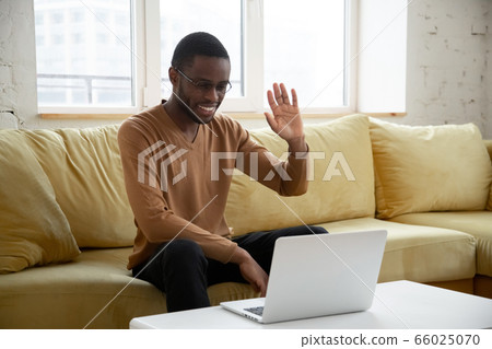 African guy sitting on couch makes videocall greeting friend 66025070
