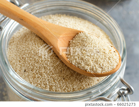 Raw uncooked fonio seeds with a spoon in a glass 66025273