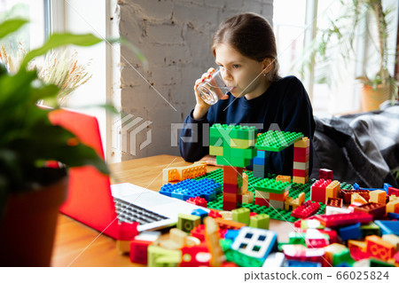 Girl playing with constructor at home, watching teacher's tutorial on laptop. Digitalization, remote education Girl playing with constructor at home, watching teacher's tutorial on laptop. Digitalization, remote education 66025824