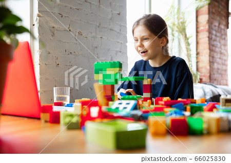 Girl playing with constructor at home, watching teacher's tutorial on laptop. Digitalization, remote education Girl playing with constructor at home, watching teacher's tutorial on laptop. Digitalization, remote education 66025830