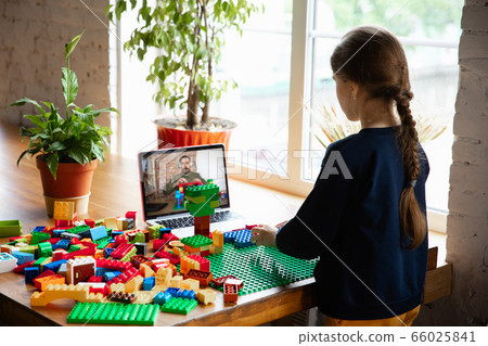 Girl playing with constructor at home, watching teacher's tutorial on laptop. Digitalization, remote education 66025841