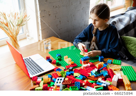 Girl playing with constructor at home, watching teacher's tutorial on laptop. Digitalization, remote education 66025894