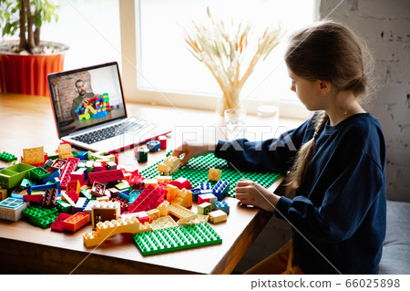 Girl playing with constructor at home, watching teacher's tutorial on laptop. Digitalization, remote education Girl playing with constructor at home, watching teacher's tutorial on laptop. Digitalization, remote education 66025898