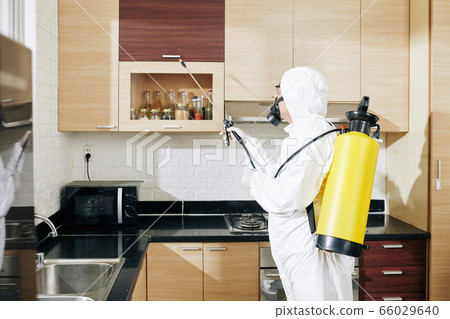 Worker in hazmat suit applying spray on surfaces 66029640