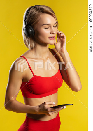 Time for music. Side view of attractive sporty blonde woman in headphones keeping eyes closed and listening music while standing against yellow background 66030840