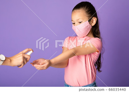 Girl in mask using sanitizer isolated over studio wall 66035440