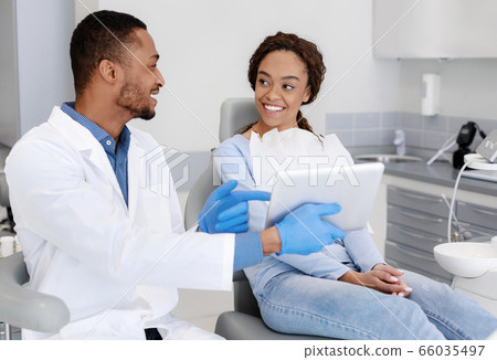 Cheery dentist showing patient clinic website on digital tablet 66035497