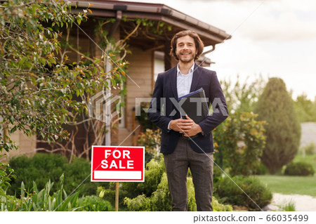 Happy real estate agent standing in front of new house for sale, outdoors. Blank space 66035499
