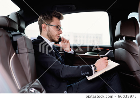 Businessman writing in notebook in luxury car Businessman writing in notebook in luxury car 66035973