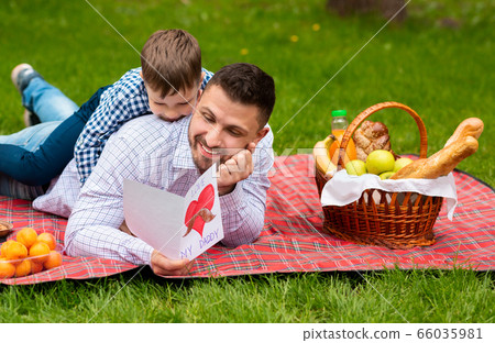 Best Father's Day greeting. Father and son with card cuddling on plaid in park during picnic Best Father's Day greeting. Father and son with card cuddling on plaid in park during picnic 66035981
