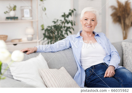 Smiling Elderly Lady Posing On Couch In Living Room At Home Smiling Elderly Lady Posing On Couch In Living Room At Home 66035982