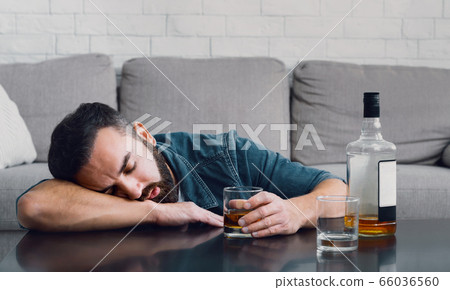 Alcohol addiction. Drunk man sleeping leaning on table with bottle and glass Alcohol addiction. Drunk man sleeping leaning on table with bottle and glass 66036560
