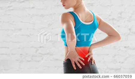 Cropped view of young woman feeling pain in her lower back after workout at gym, copy space Cropped view of young woman feeling pain in her lower back after workout at gym, copy space 66037059