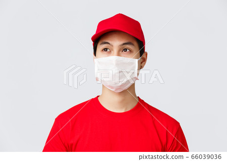 Covid-19, self-quarantine online shopping and delivery concept. Thoughtful young asian courier working during coronavirus outbreak to bring orders client doorstem, wear medical mask and uniform 66039036
