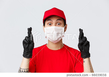 Covid-19, self-quarantine online shopping and delivery concept. Nervous asian courier in medical mask and protective gloves, wear uniform, cross fingers praying, hoping something fulfill 66039038