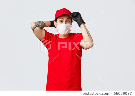 Nervous asian delivery guy hurry up deliver goods, put on red cap uniform, medical mask and protective gloves, shipping parcels during covid-19 pandemic. Concept of online shopping and self-isolation Nervous asian delivery guy hurry up deliver goods, put on red cap uniform, medical mask and protective gloves, shipping parcels during covid-19 pandemic. Concept of online shopping and self-isolation 66039087