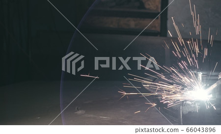 Forge workshop. Smithy. Worker in a welding hood helmet welds a part by electric welding. Sparks are reflected in the protective screen. Forge workshop. Smithy. Worker in a welding hood helmet welds a part by electric welding. Sparks are reflected in the protective screen. 66043896