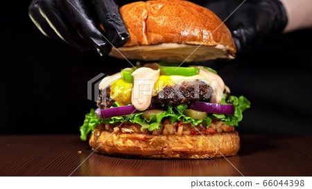 Craft burger is cooking on black background. Consist: sauce salsa, lettuce, red onion, pickle, cheese, chilli green pepper, bun, marbled meat beef. Craft burger is cooking on black background. Consist: sauce salsa, lettuce, red onion, pickle, cheese, chilli green pepper, bun, marbled meat beef. 66044398