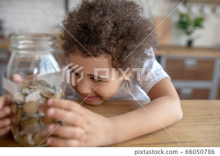 Cute curly-haired kid in a white tshirt holding a moneybank Cute curly-haired kid in a white tshirt holding a moneybank 66050786